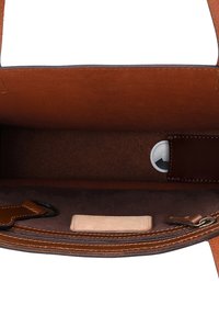 Borsa aperta in pelle marrone che mostra l'interno in morbida pelle scamosciata, piccola pochette in pelle contenente un dispositivo di localizzazione wireless bianco.