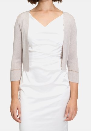 Kvinde iført en hvid ærmeløs kjole med en lysegrå cropped cardigan med trekvartærmer og dekorative kanter.