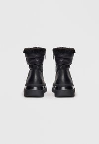 Zwarte enkelboots met een glanzende afwerking, een opgeblazen schacht met nepbont trim, en een dikke, textuur-gevoelige zool voor extra comfort.