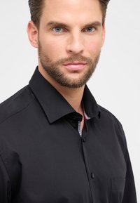 Camicia nera con bottoni, dotata di un colletto strutturato, caratterizzata da un interno a fantasia contrastante e da una tasca sul lato sinistro.