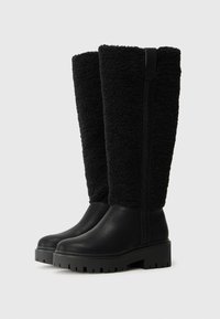 Botas negras hasta la rodilla con un upper texturizado y de felpa y un lower de cuero liso. Cuenta con una suela gruesa con relieve y detalles en la costura lateral.