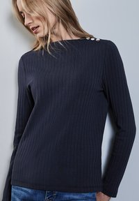Maglia a maniche lunghe a coste blu marina con scollo a barca e tre bottoni decorativi sulla spalla sinistra, realizzata in un morbido tessuto testurizzato.