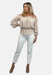 Beżowa bluzka z odkrytymi ramionami, z bufkami na rękawach i falbaną na dole, zestawiona z białymi dopasowanymi spodniami i obcasami w wężowy wzór.