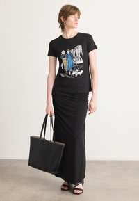 Black t-shirt with graphic print, paired with a black ruched skirt and black strappy sandals. Holding a black tote bag with embossed logo.