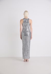 Robe en sequins argentés avec une silhouette ajustée, un design sans manches, un col montant et une jupe longue, présentant une texture lisse et réfléchissante.