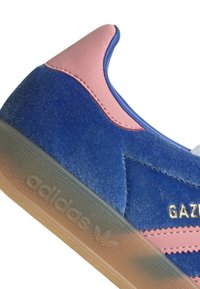 Μπλε σουέτ αθλητικά παπούτσια με ροζ δερμάτινες λεπτομέρειες, διαθέτοντας γόμα καουτσούκ, υφή στην επιφάνεια και χρυσό κείμενο "GAZELLE" στο πλάι.