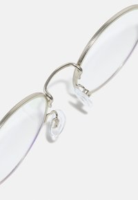Ochelari de vedere din metal argintiu, cu lentile rotunde, având un design texturat, tăciuni de nas transparente și o estetică minimalistă.