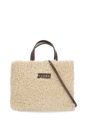 Borsa a mano in shearling beige strutturato con manici corti marroni e tracolla lunga marrone, con una piccola toppa rettangolare con logo.