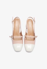 Chaussures slingback en cuir verni rose clair, avec un bout arrondi blanc et une fine sangle de cheville avec une boucle réglable.