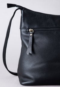Black leather shoulder bag with a textured finish, featuring a zippered pocket and a slender shoulder strap. Accented with a small leather tassel.