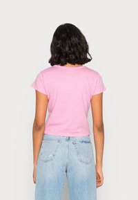 Camiseta corta de algodón rosa con escote redondo y mangas cortas, diseño recortado, combinada con jeans desgastados de color azul claro.