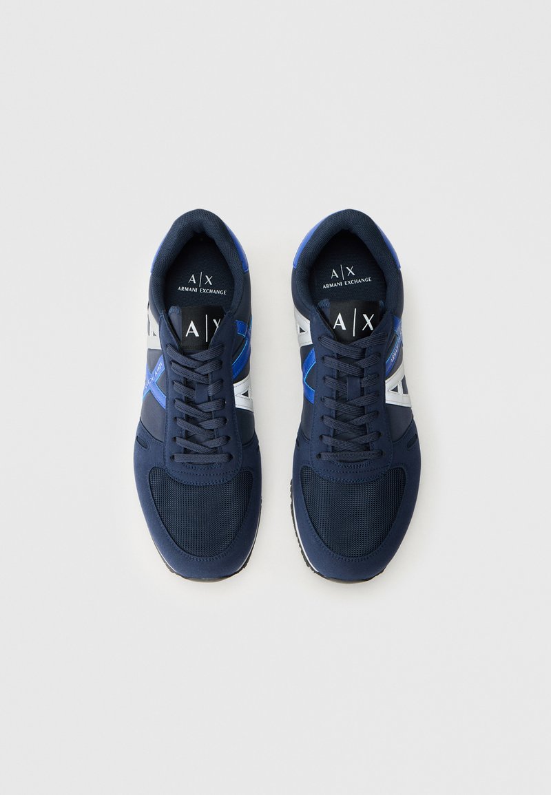 Zapatillas deportivas azul marino con parte superior de malla y tejido sintético, acentos en blanco y azul en contraste, punta redonda y cierre con cordones.