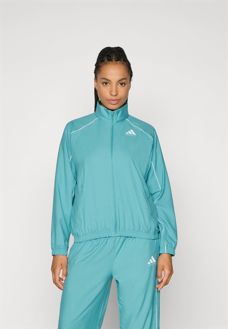 Tyrkysová športová bunda s vysokým golierom, elastickým pásom a bielymi pruhmi. Obsahuje logo Adidas na hrudi.