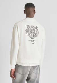 Sudadera de algodón blanca con un gráfico de tigre negro en la espalda, puños y dobladillo acanalados, corte relajado y cuello de tripulación.