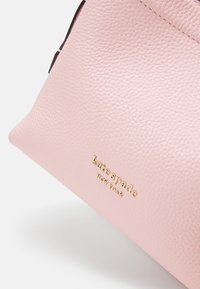 Borsa in pelle rosa chiaro con superficie testurizzata, caratterizzata da un logo dorato con la scritta "kate spade NEW YORK" nella parte inferiore.