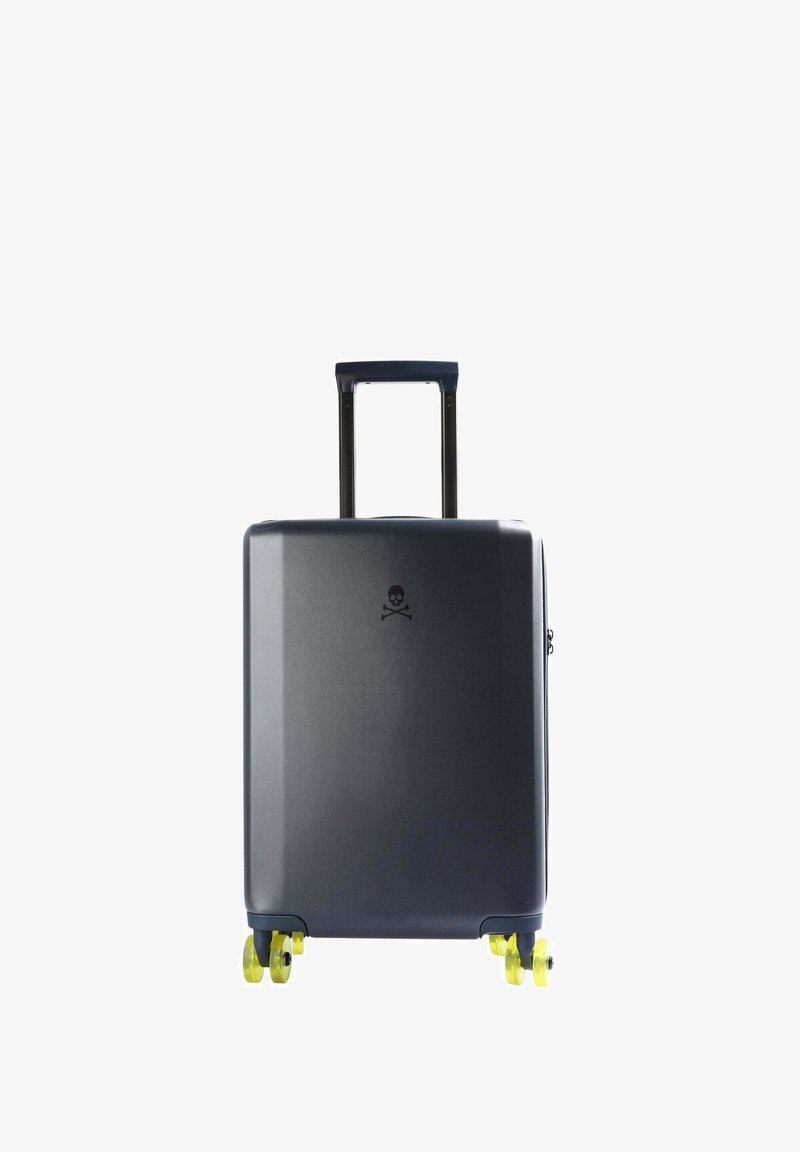 Maleta rígida de color gris oscuro con un acabado mate. Cuenta con un mango retráctil, cuatro ruedas amarillas y un logotipo de calavera. Diseño compacto.