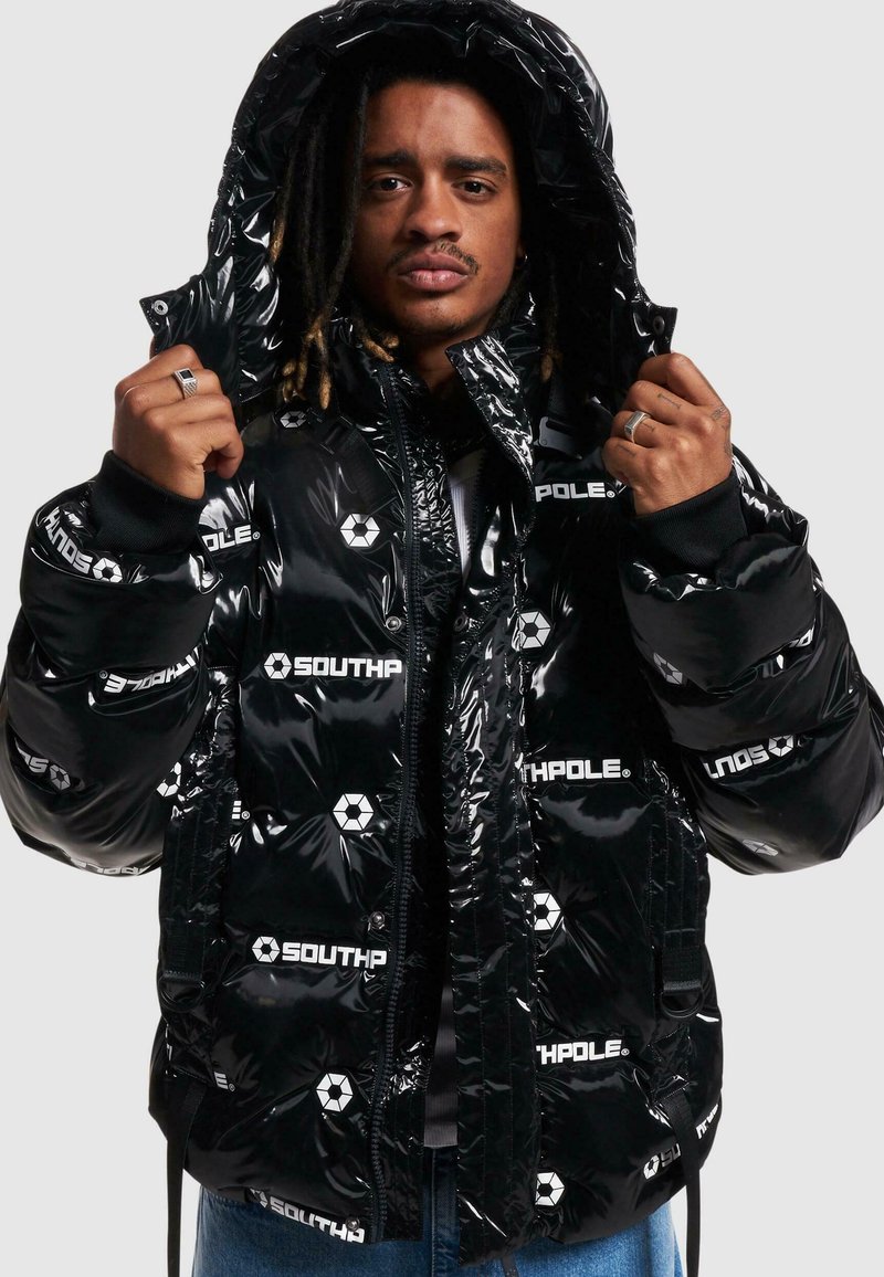 Geacă puffer neagră cu o finisare lucioasă, având logo-uri albe "SOUTHPole", glugă detașabilă și manșete ribbate. Silueta este confortabilă.