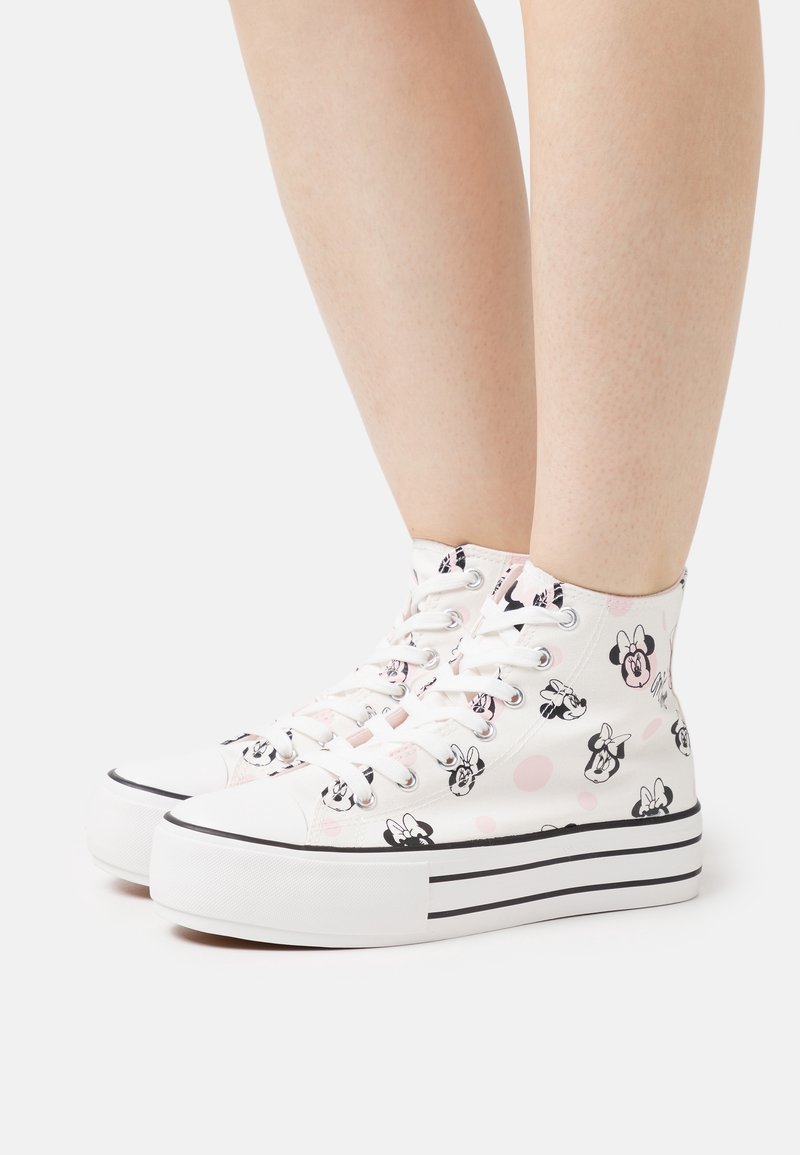 Vita plattformshigh-top sneakers med svarta och rosa Minnie Mouse-ansikten och ljusrosa prickar, bärs på bara ben.