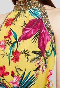 Bright yellow halter neck dress featuring a floral print with pink, purple, and green leaves. Contains a patterned band at the collar.