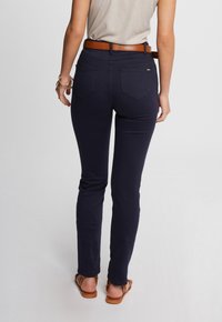 Jeans en denim stretch bleu marine avec une coupe ajustée, dotés de poches arrière et d'une ceinture en cuir marron. Texture lisse, coupe slim.