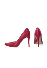 Červené kožené lodičky na vysokém podpatku s špičatou špičkou, zvýšeným jehlovým podpatkem a malým dekorativním zlatým emblémy na zadní straně.