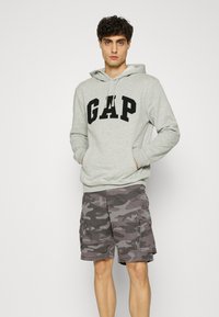 Light gray hoodie featuring a prominent black "GAP" logo, paired with gray camo cargo shorts with multiple pockets and a relaxed fit.