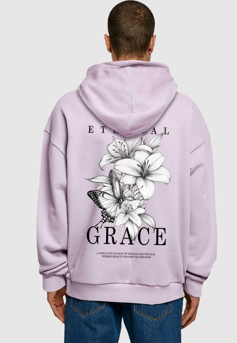 Lila Kapuzenpullover mit einem großen schwarz-weißen Blumenmuster, das Lilien und einen Schmetterling auf dem Rücken zeigt. Der Text lautet "EWIGE GNADE."