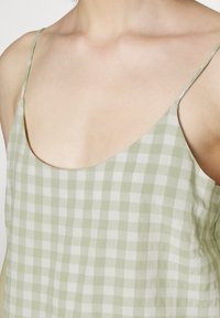 Top em xadrez verde e branco com finas alças de espaguete e um decote largo, feito de um tecido leve com uma textura suave.