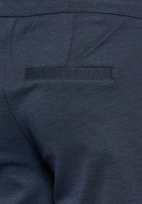 Marineblauwe stofbroek met een gladde, gestructureerde oppervlakte, een enkele achterzak en zonder zichtbare sluitingen of versieringen.