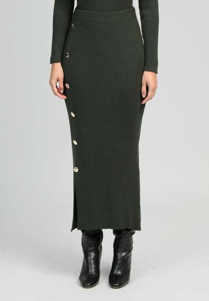 Jupe tricotée côtelée vert foncé avec des accents de boutons sur le côté, dotée d'une fente et d'une coupe ajustée, associée à des bottines noires.