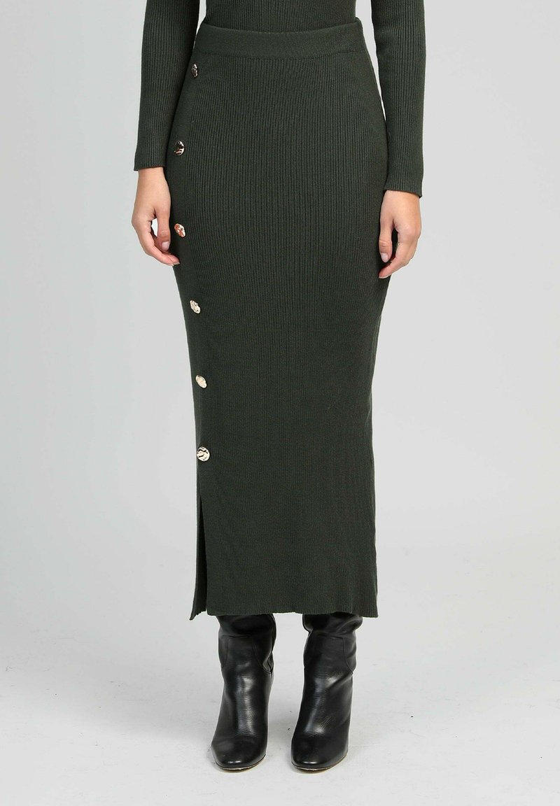 Jupe tricotée côtelée vert foncé avec des accents de boutons sur le côté, dotée d'une fente et d'une coupe ajustée, associée à des bottines noires.