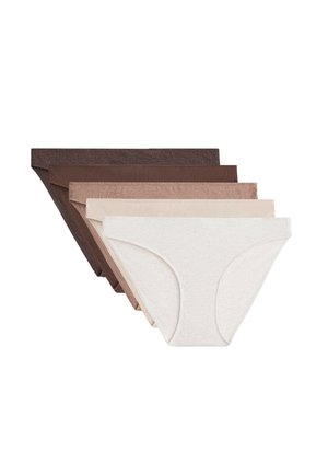 Femme portant un sous-vêtement bikini en coton uni de couleur claire, montrant la taille et la partie supérieure de la cuisse sur fond blanc.
