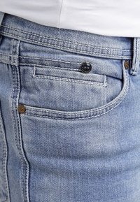 Vaqueros de mezclilla azul claro con textura suave, que cuentan con un bolsillo trasero, costuras en contraste y un botón metálico circular con el año "1978".