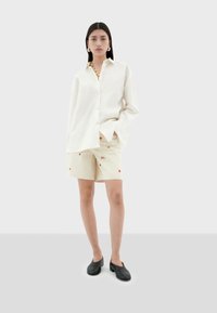 Witte overhemden met lange mouwen, gecombineerd met beige shorts met rode geborduurde bloemen en zwarte schoenen. Minimalistisch ontwerp.