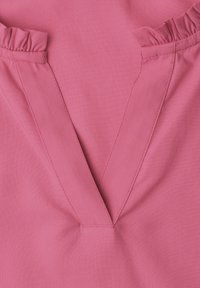 Close-up of pink fabric with a V-shaped neckline and small gathered ruffles at the top edges.