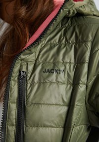 Groene pufferjack met een roze capuchon, voorzien van een zwarte ritssluiting en logo. De stof heeft een gewatteerde textuur met een lichte glans.