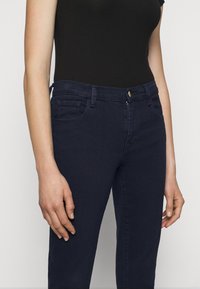 Mörkblå denim jeans med en figurnära design, klassisk femfickstil och framknäppning. Mjuk textur med en lätt stretch.