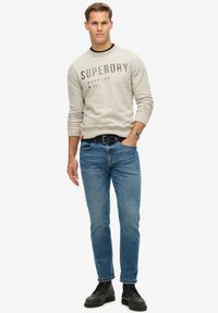 Grijze sweatshirt met "SUPERDRY" opdruk, blauwe jeans en zwarte laarzen. Slim fit, ronde halslijn, met ribgebreide manchetten en tailleband.