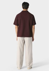 Camicia corta a maniche corte color mogano con tessuto testurizzato, abbinata a pantaloni larghi beige chiaro. Design minimalista, senza motivi visibili.