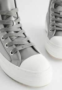 Hallid kõrged hallid sneakers, mis on valmistatud siledast kangast, valge kummist varbakaitsega, lamehallide paelte ja hõbedaste silmadega. Paks valge tald.