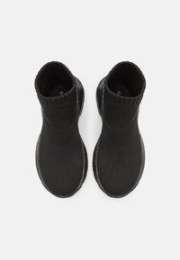 Černé kotníkové boty s ribovaným textilním svrškem, elegantním tvarem a gumovou podrážkou. Design zdůrazňuje moderní, minimalistickou estetiku.