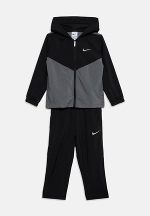 Czarna i szara kurtka z kapturem Nike z zamkiem błyskawicznym oraz pasujące czarne spodnie, oba z białymi logo Nike swoosh.