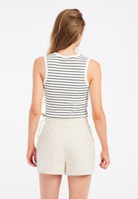 Striped sleeveless top in white and black, paired with light beige shorts. The top features a fitted design and a high neckline.