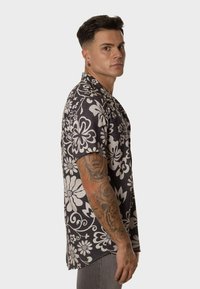 Camisa de manga corta en blanco y negro con un ajuste relajado, que presenta un cuello con solapa y una textura sutil. Con acentos de flores blancas por todo el diseño.