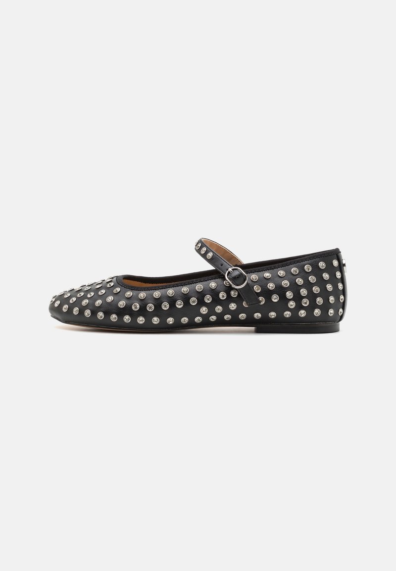 Chaussure plate Mary Jane noire avec des clous argentés partout et une bride à boucle sur le dessus, sur un fond uni clair.