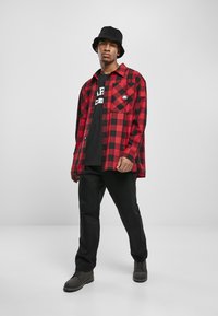 Rød og sort ternet flannel skjorte med to lommer, parret med en sort grafisk t-shirt og sorte bukser. Sort bøttehat og støvler.