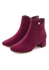 Burgunderfarbene Stiefeletten aus Wildleder, mit runder Zehenpartie, niedrigem Blockabsatz und einem kleinen goldenen Akzent nahe der oberen Kante. Glatte Textur.