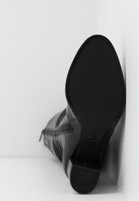 Bottine en cuir noir avec bout arrondi, dessus texturé, fermeture éclair latérale et semelle plate. Logo de la marque sur le talon.