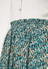 Jupe en teal à motifs avec une taille élastique. Présente un mélange de designs à taches noires, crème et marron. Tissu doux et silhouette évasée.