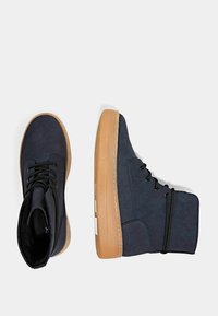 Scarpe alte di colore blu navy realizzate in suede con suola in gomma, dotate di lacci neri e minimi accenti bianchi sul lato.